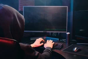 Ilustración que representa estafas por internet: figura en capucha frente a ordenador y símbolos de fraude digital.